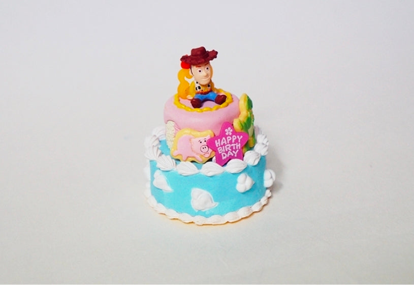 Mini birthday cake toy with Woody figure on top, blue frosting and “Happy Birthday” banner
