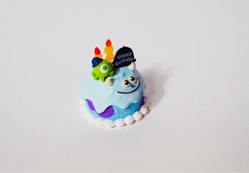 Mini birthday tart figure with green Mike Wazowski topper on light blue frosted cake