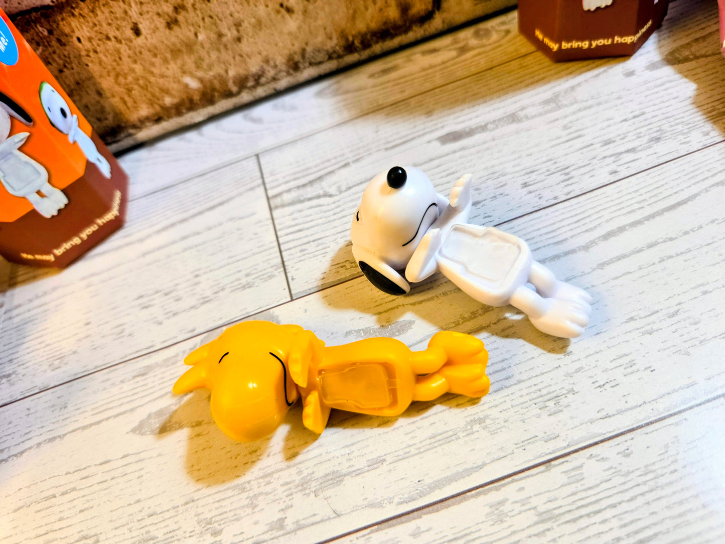 Mini vinyl character figures on light wood floor: yellow figure reclining, white figure reaching