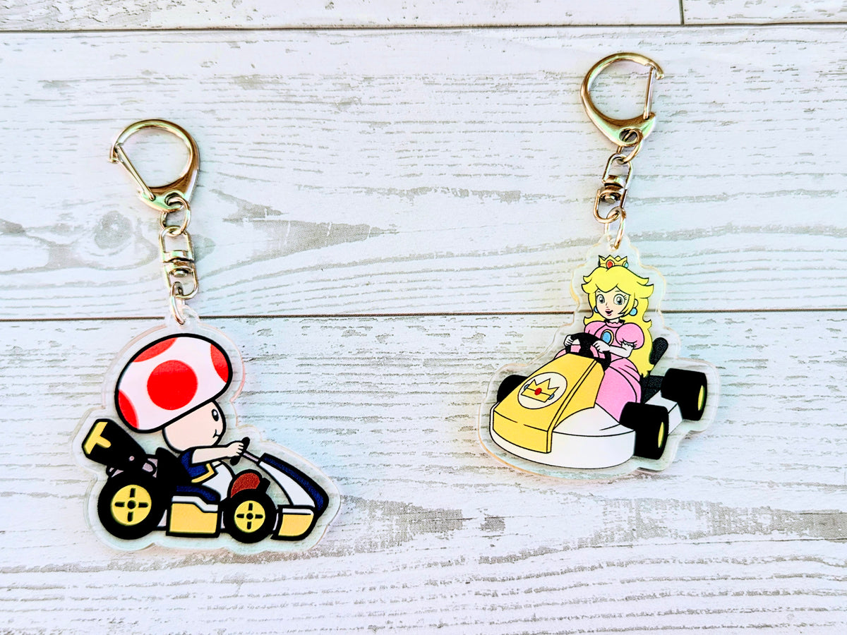 Set of two acrylic die-cut keychains with gold keyrings: Toad kart and Peach kart