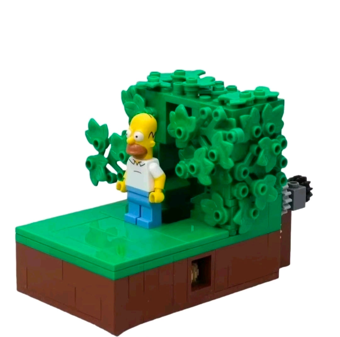 Brick playset with dark green foliage, brown base, and Homer-style minifigure on platform.