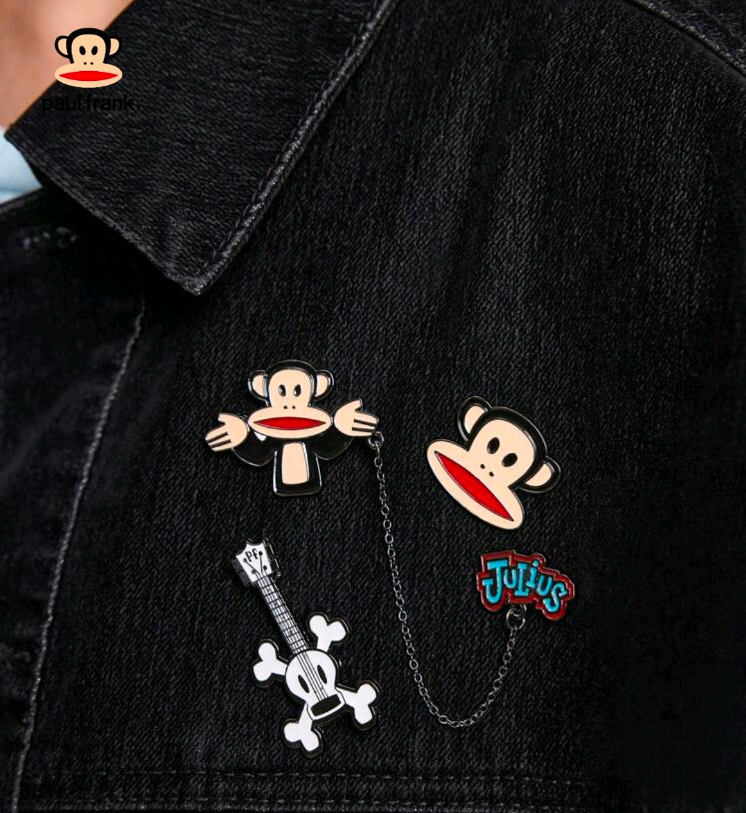 Enamel pins on black denim jacket: Julius monkey face, guitar bone, and Tutius pin