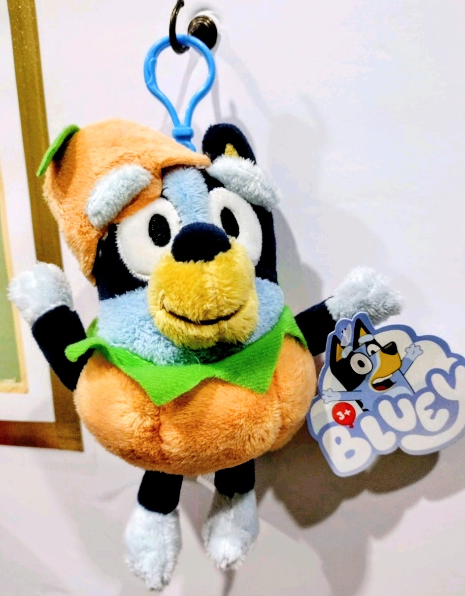 Light blue and black Halloween plush keychain with green vest, smiling face, and tag