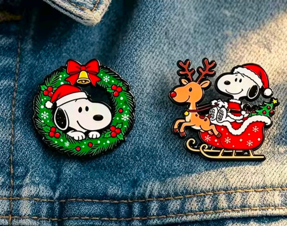 Snoopy Christmas enamel pins on denim: wreath pin and sleigh reindeer pin