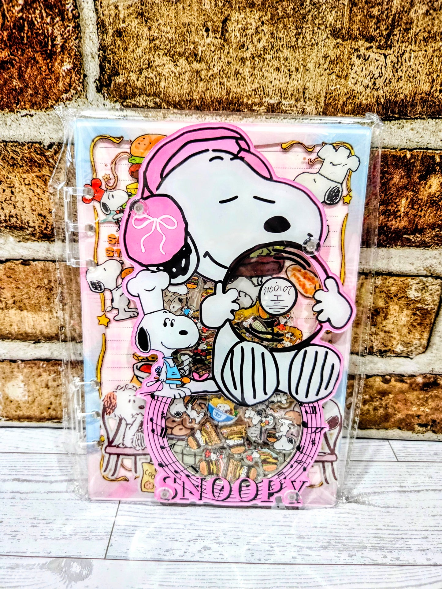 A5 acrylic shaker notebook with Snoopy chef and food collage on a pink cover in clear sleeve.