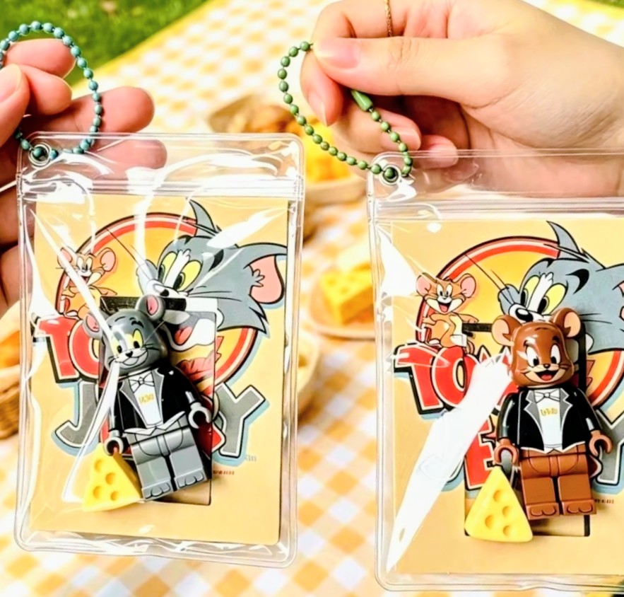 Close-up of two clear keychain pouches with bead loops, gray Tom and brown Jerry designs