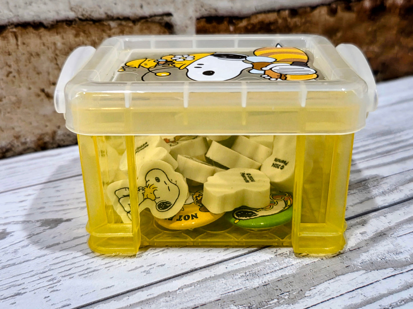 Yellow desktop organizer box with clear lid filled with Snoopy character erasers