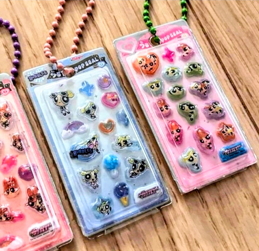 Two character 3D resin keychain blister packs with bead necklaces on wooden surface
