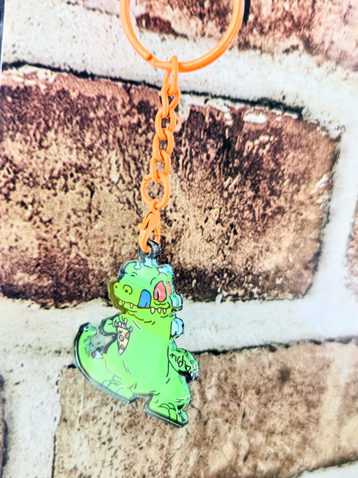 Orange-ring acrylic keychain featuring a green Reptar sitting figure on orange chain