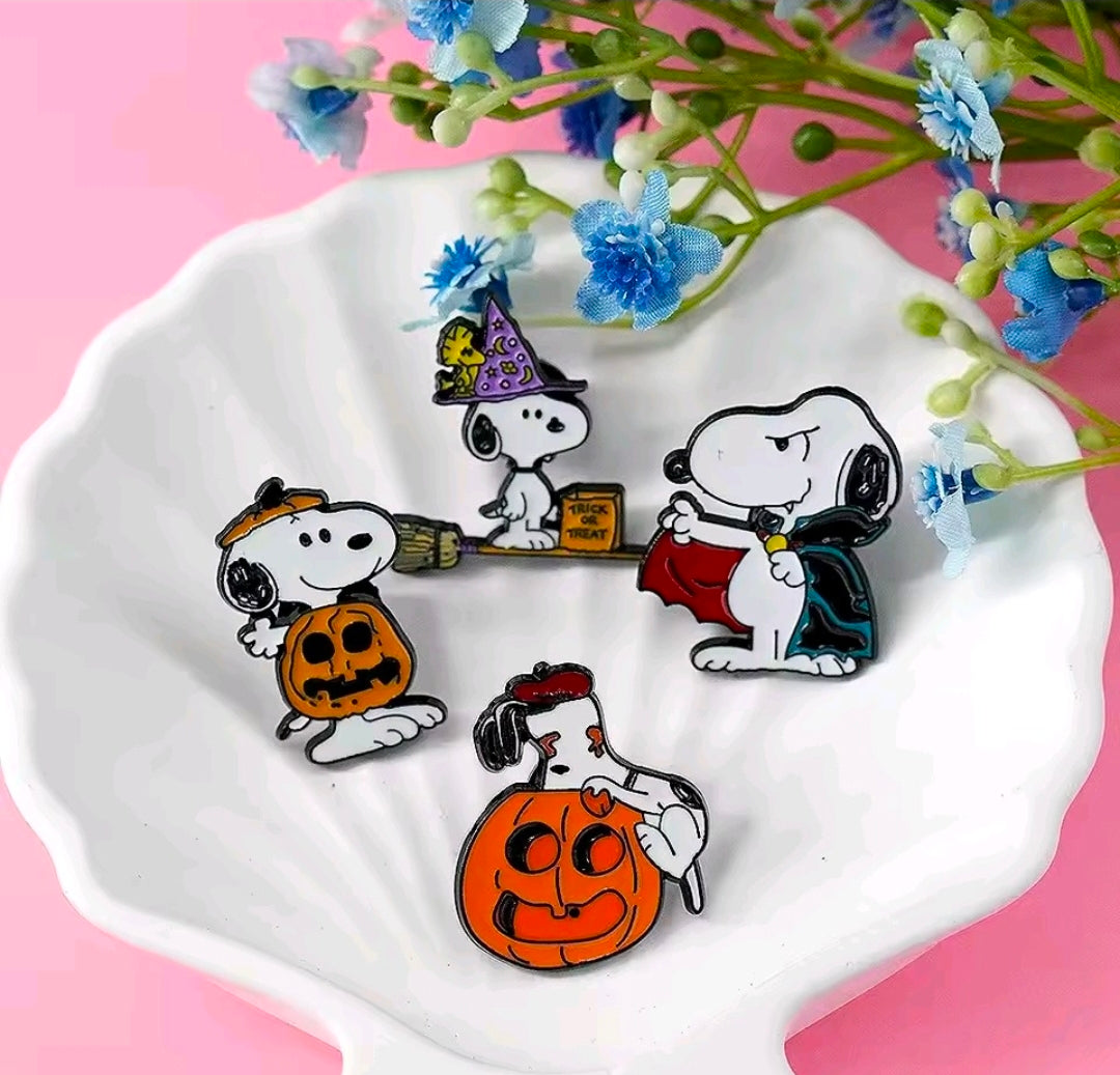 Snoopy Halloween enamel pin set on a white dish, showing ghost, pumpkin, witch, and bat pins.