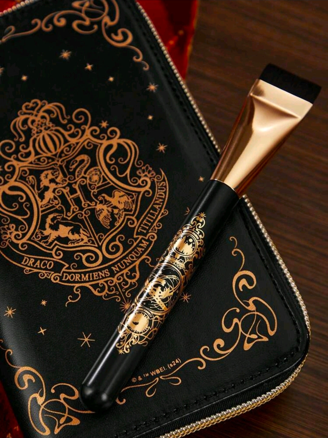 Black zippered brush case with gold crest design and gold-handled makeup brush inside