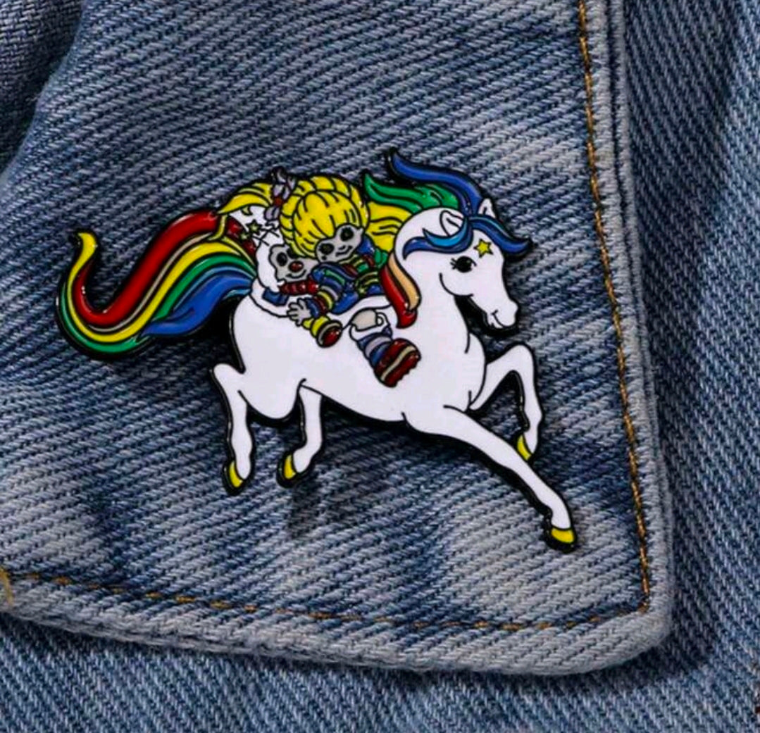 Enamel riding duo pin on blue denim, depicting blond girl riding a white horse