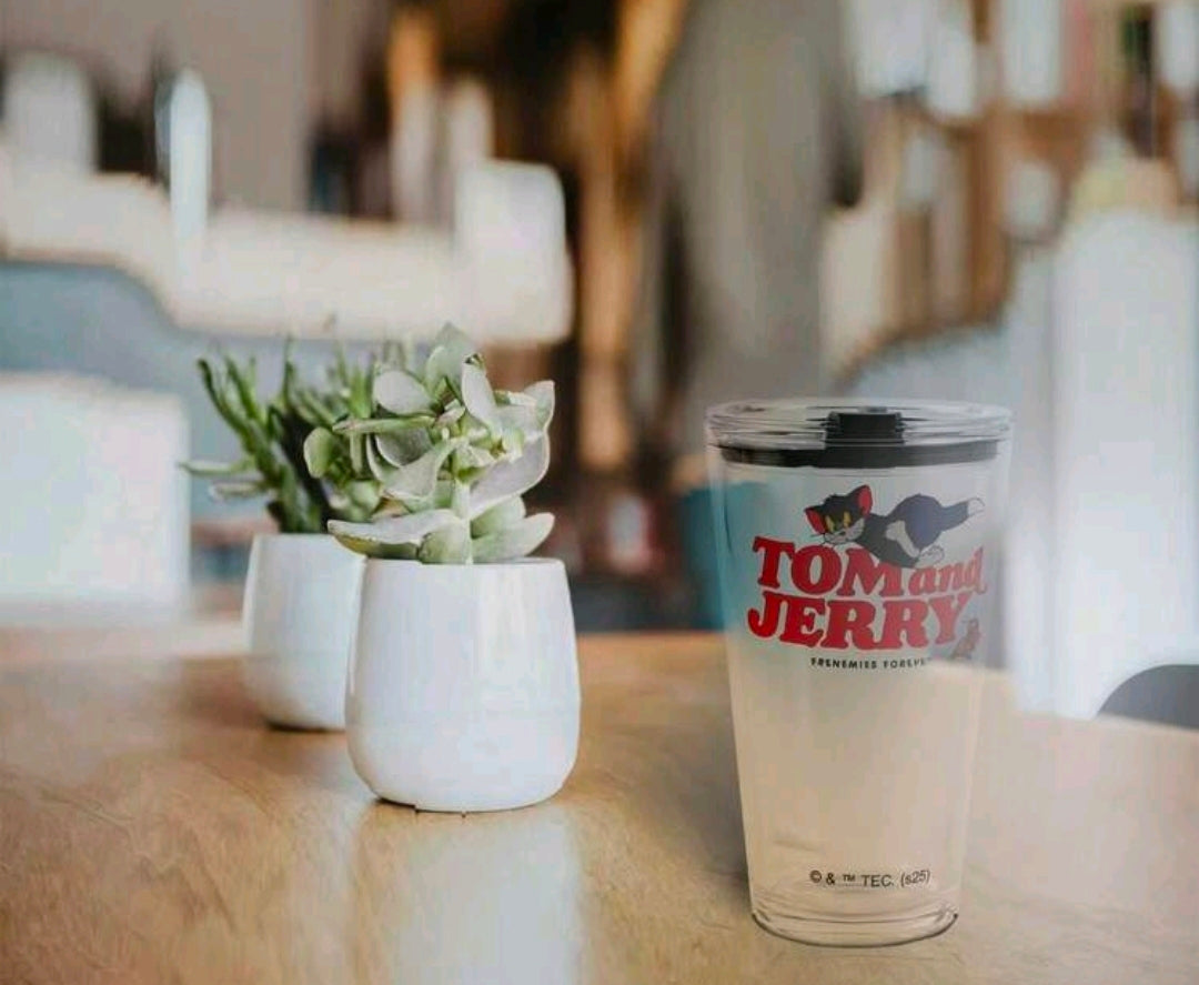 Clear tumbler with Tom and Jerry graphic and black lid on wooden table