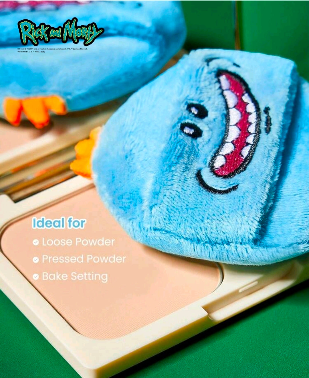 Triangular plush blue powder puff with stitched grinning cartoon face, orange trim, on makeup palette.