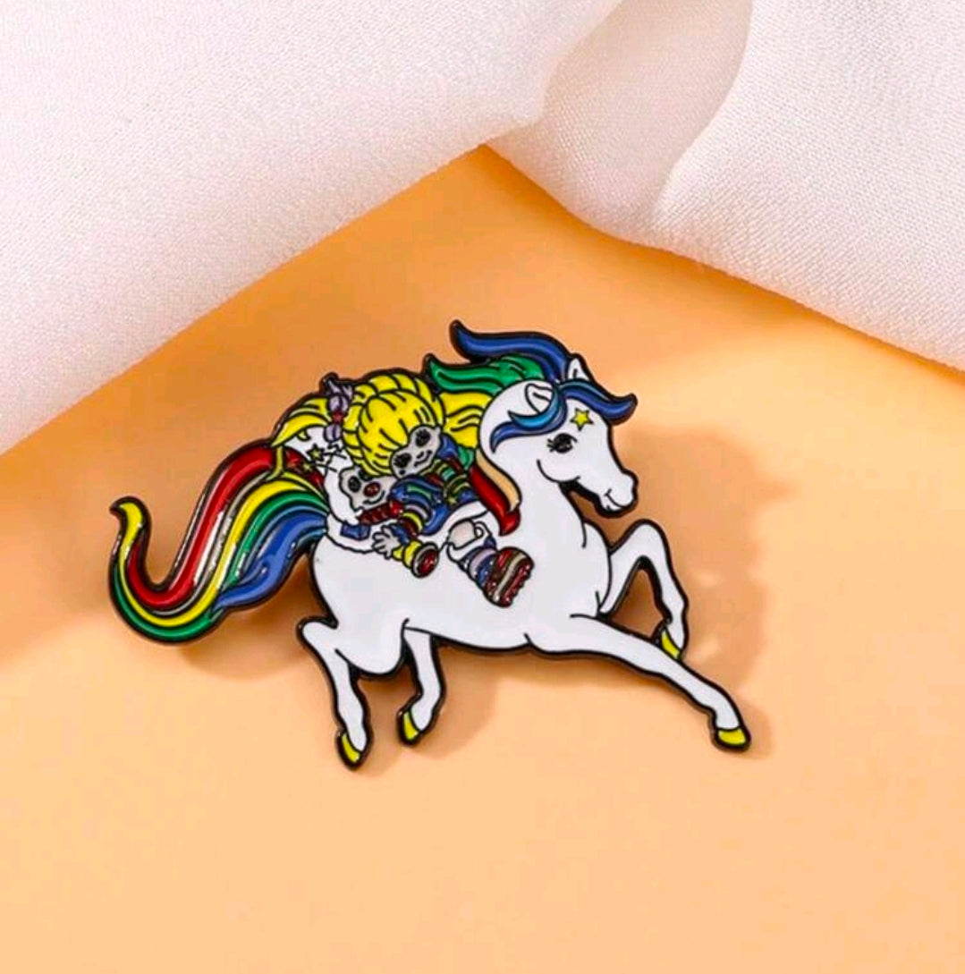 Enamel riding duo pin on peach fabric, blond girl on a white horse with rainbow mane
