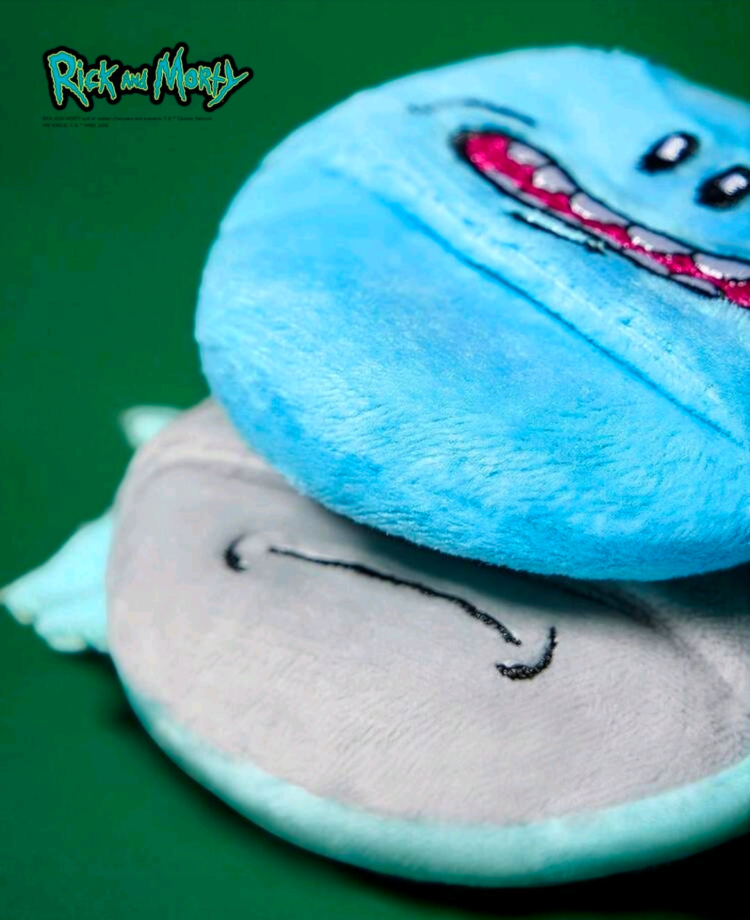 Close view of stacked round plush powder puffs: blue on top, gray beneath, stitched eyes.
