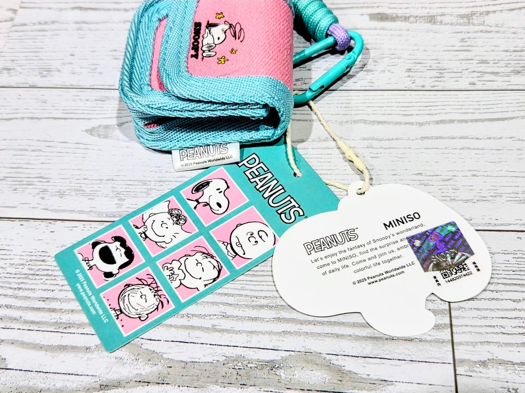 Teal canvas earbud case with flap and carabiner, Snoopy patch, paper tags nearby