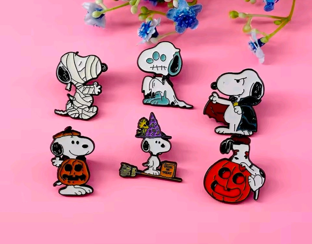 Six Snoopy Halloween enamel pins on a pink background, featuring ghost, pumpkin, witch and bat.