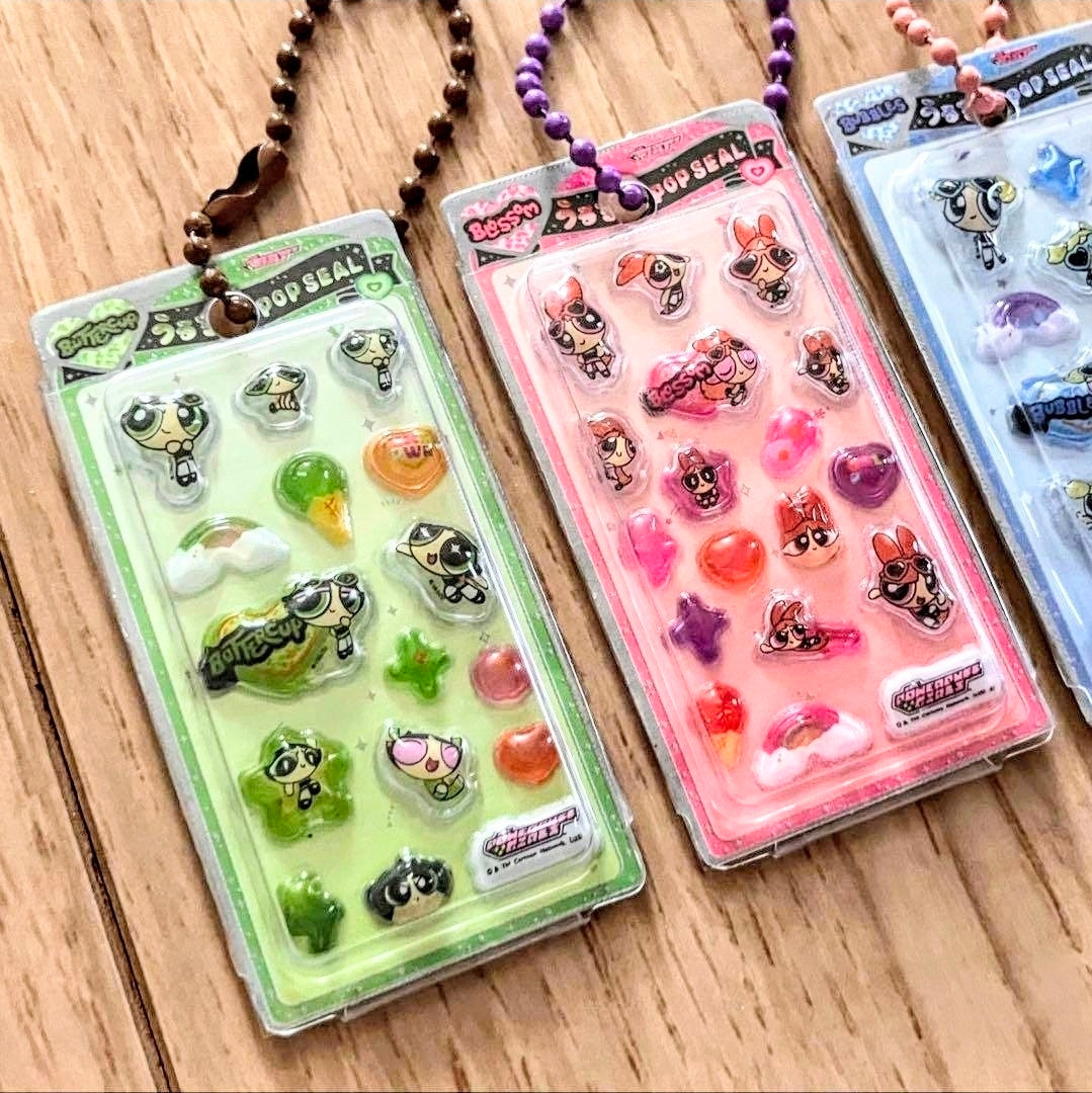 Three character 3D resin keychain blister packs with bead necklaces on wooden surface