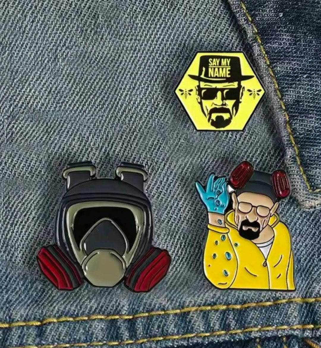 Two enamel pins on denim: gas mask and “Say My Name” hexagon portrait