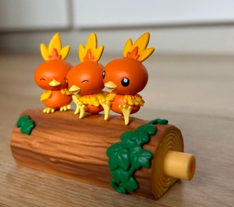 Torchic trio toy figures standing on a brown log with green leaf decorations.