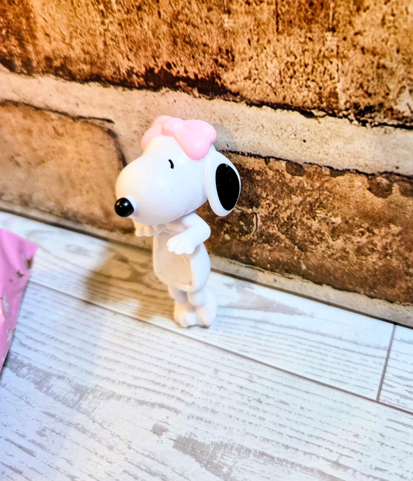 White mini figure with pink bow, large black nose, looking left