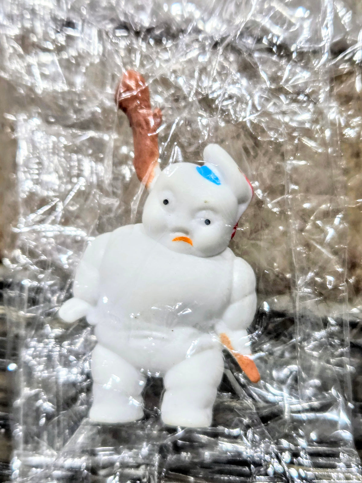Toy mini figure with orange roasted-marshmallow stick, white body, sealed in clear plastic