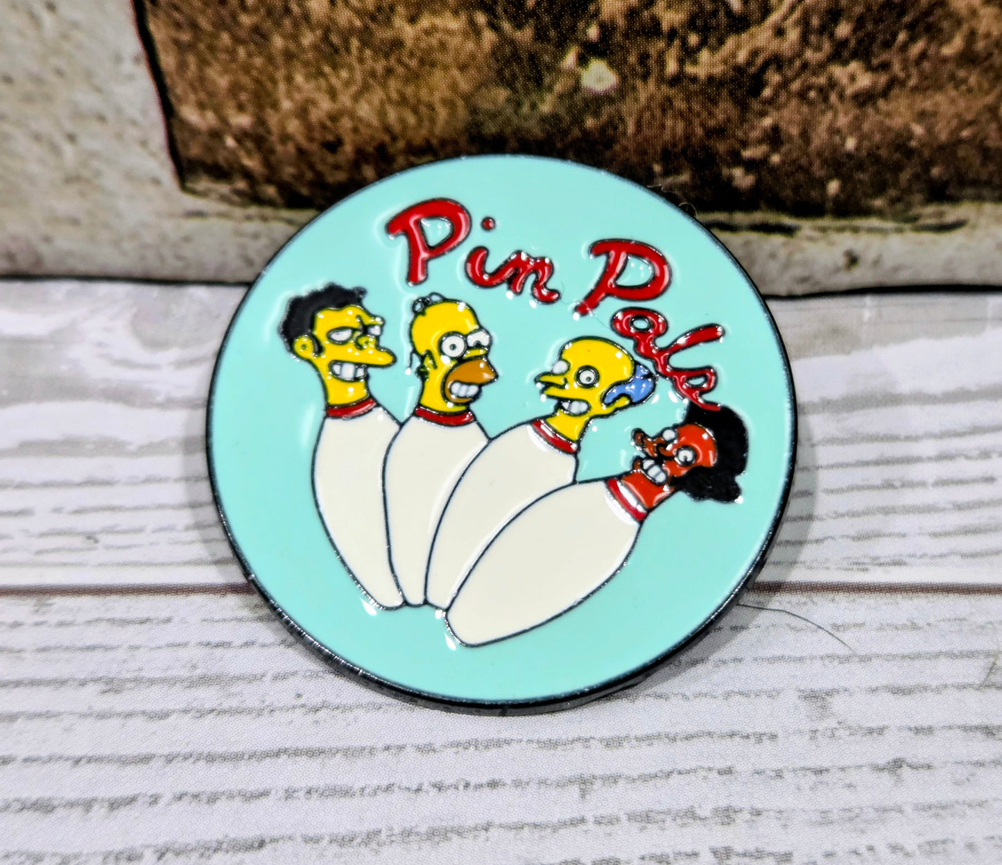 turquoise round enamel pin with three Simpsons characters and red 'Pin Pals' text