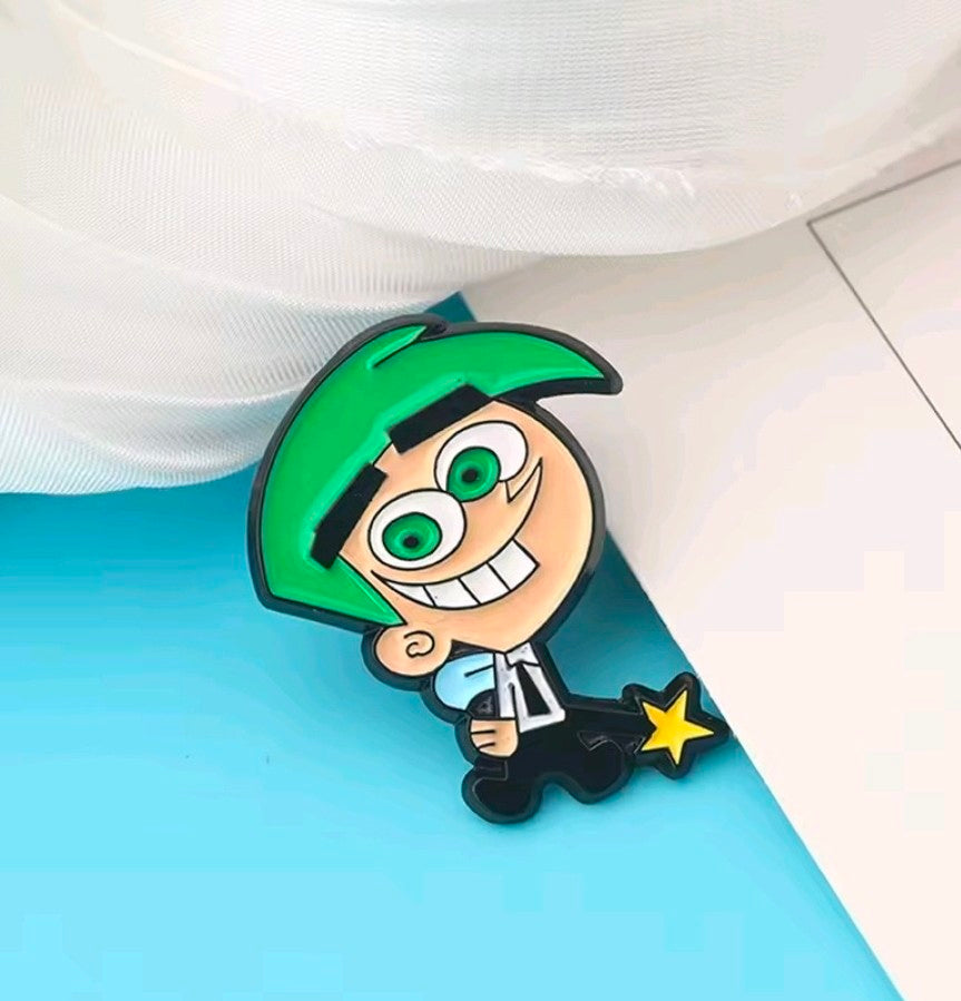 Timmy enamel pin with green cap, big eyes, blue shirt, and gold star charm.