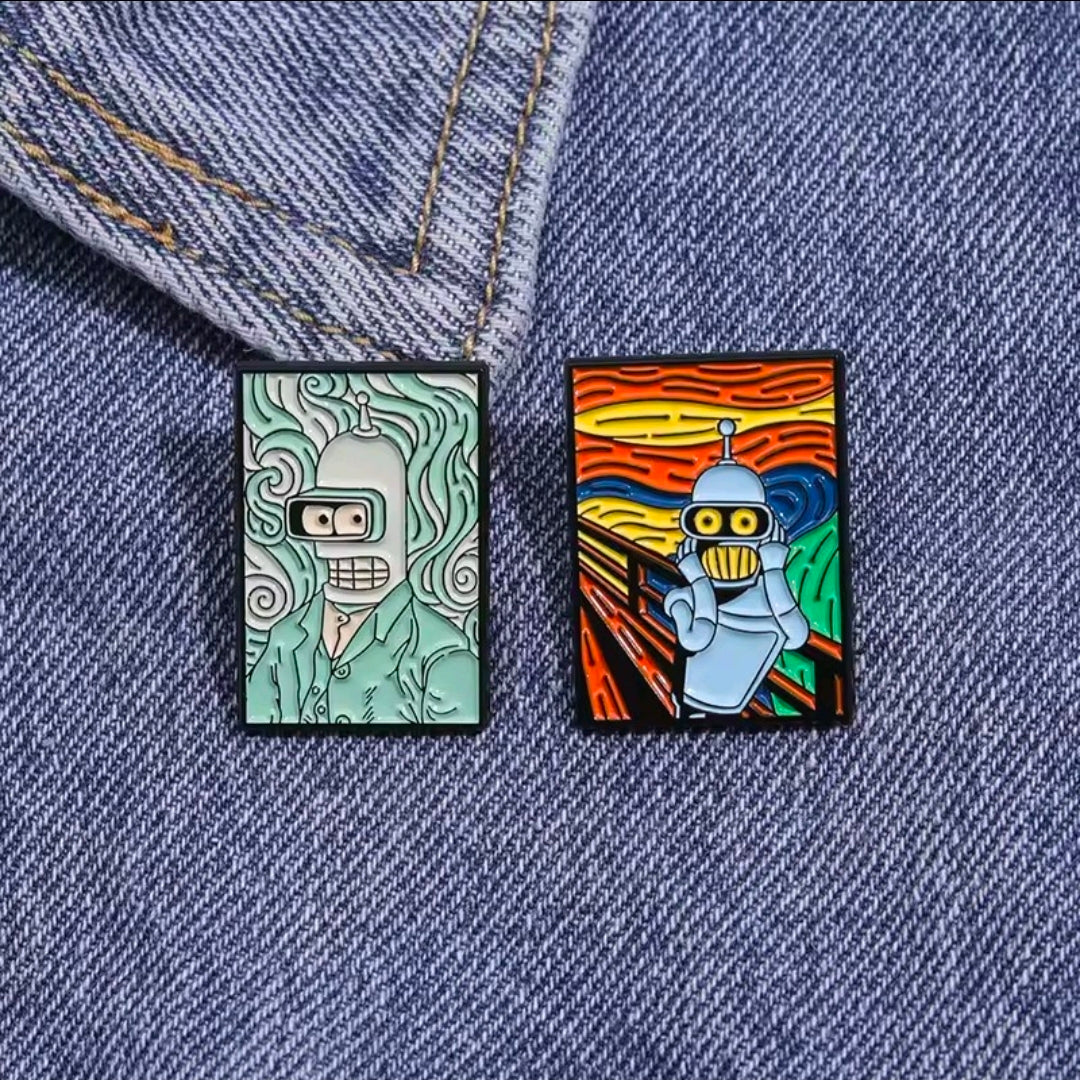 Two square enamel pins on denim: left teal robot face and right orange robot