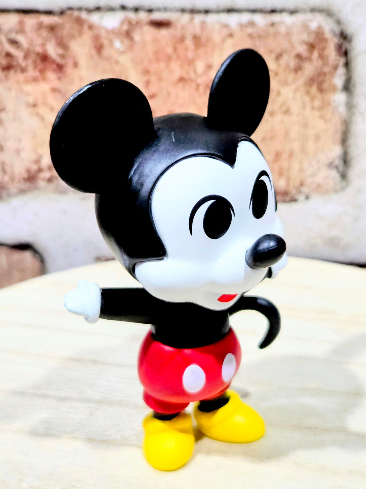 Mickey Mouse vinyl figure holding a white accessory, red outfit and yellow shoes.