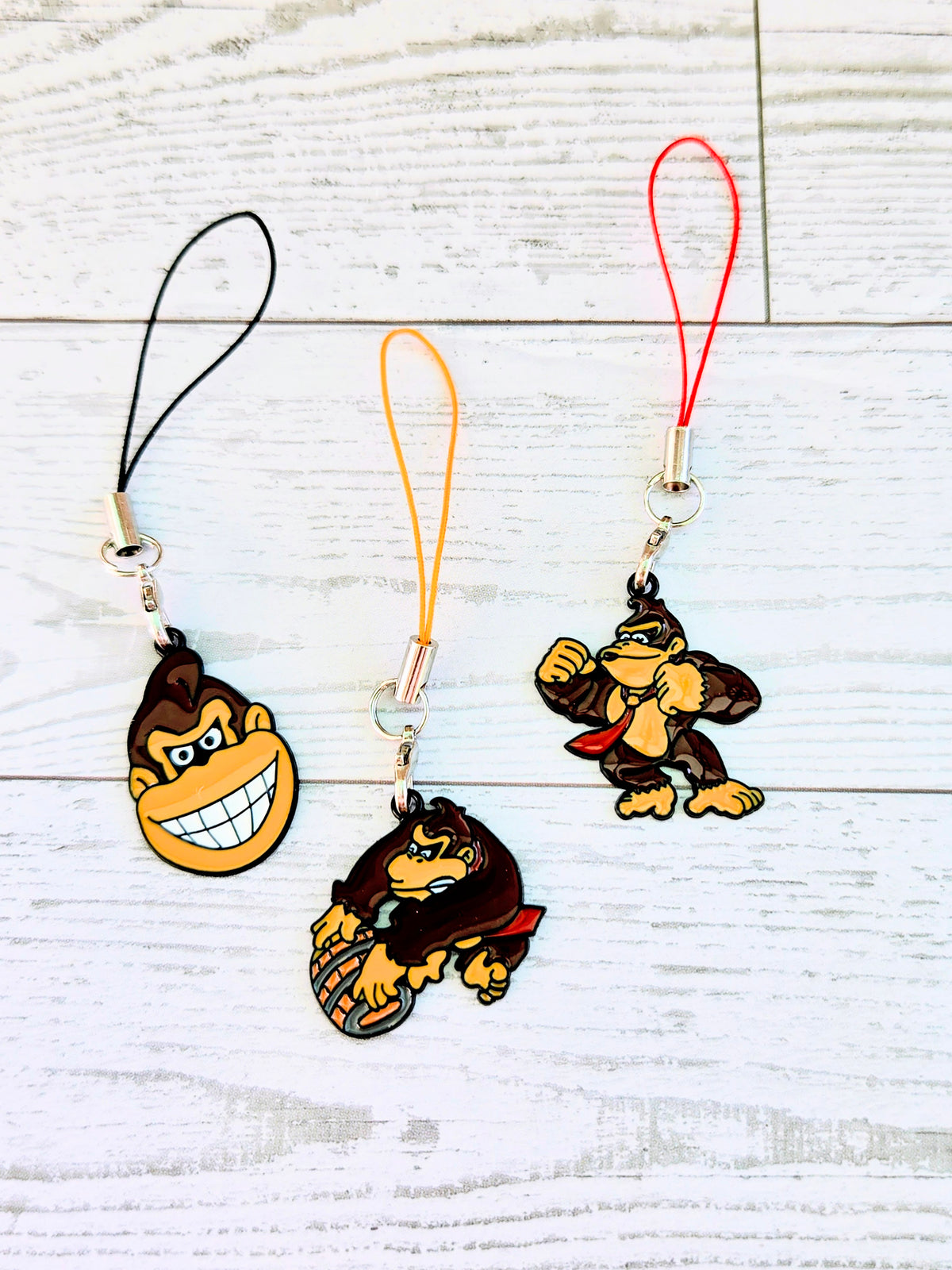Set of 3 phone charm wrist straps with black, orange, and red cords and charms