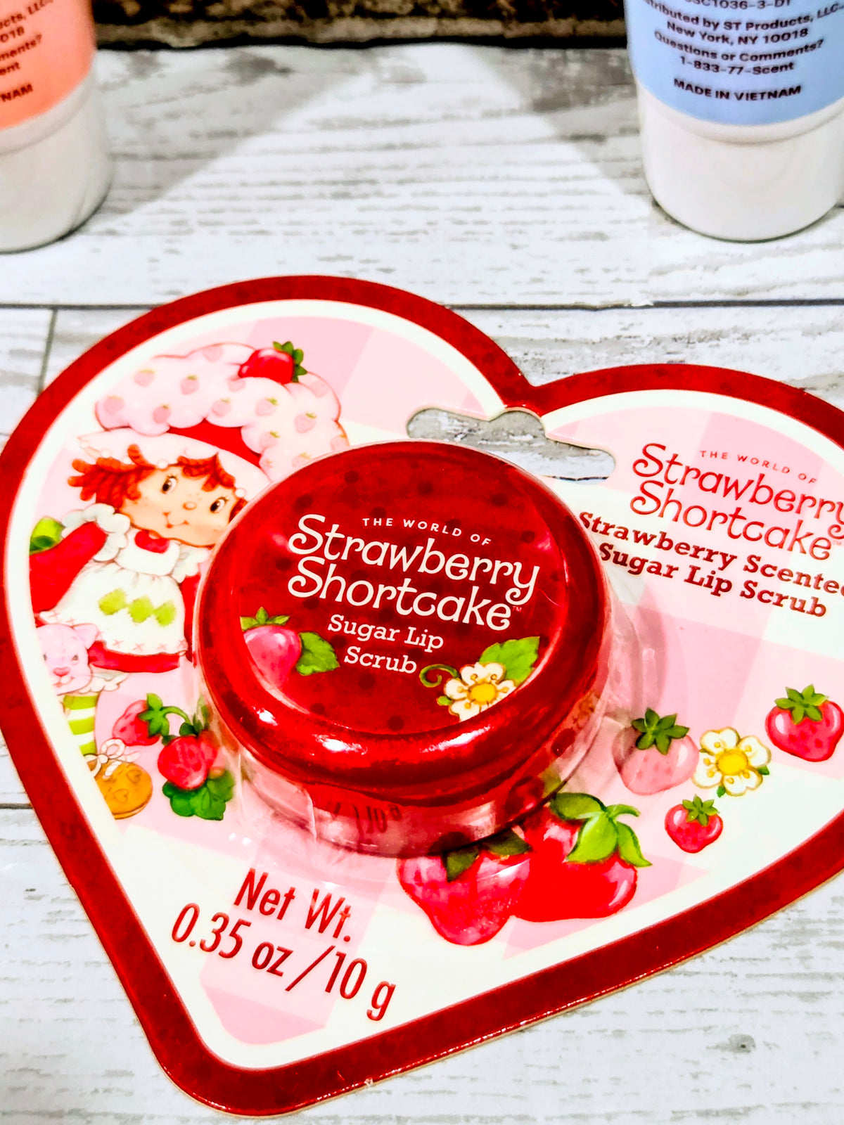 Heart package holding red Strawberry Shortcake sugar lip scrub jar with strawberry graphics