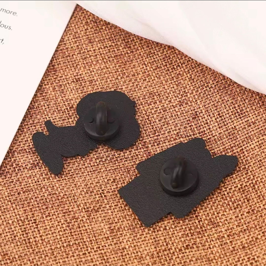 Two black enamel pins with butterfly clutch backs and dark textured finish