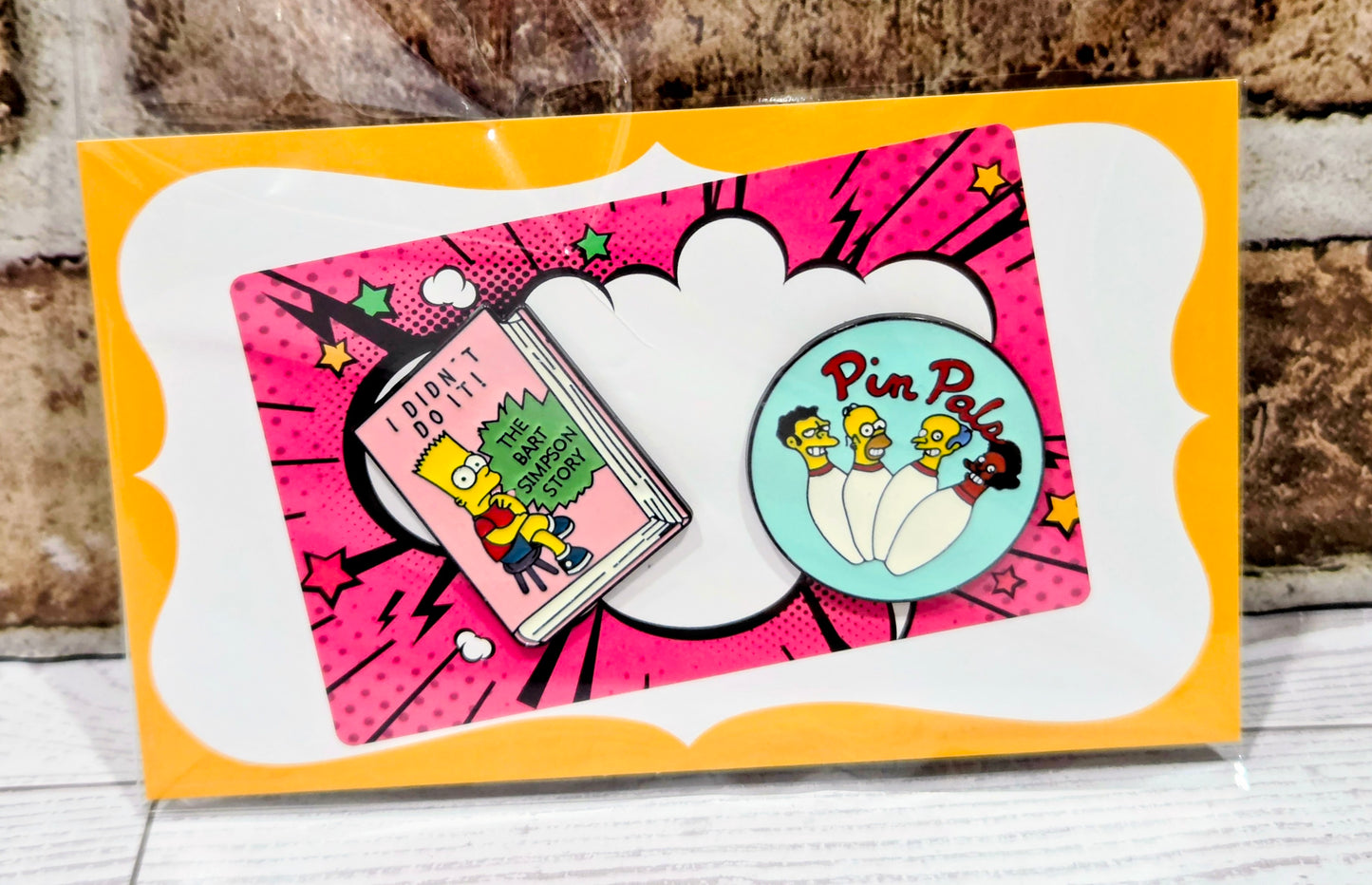 Simpsons enamel pin set on orange card with round Pin Pals pin and pink book-shaped pin