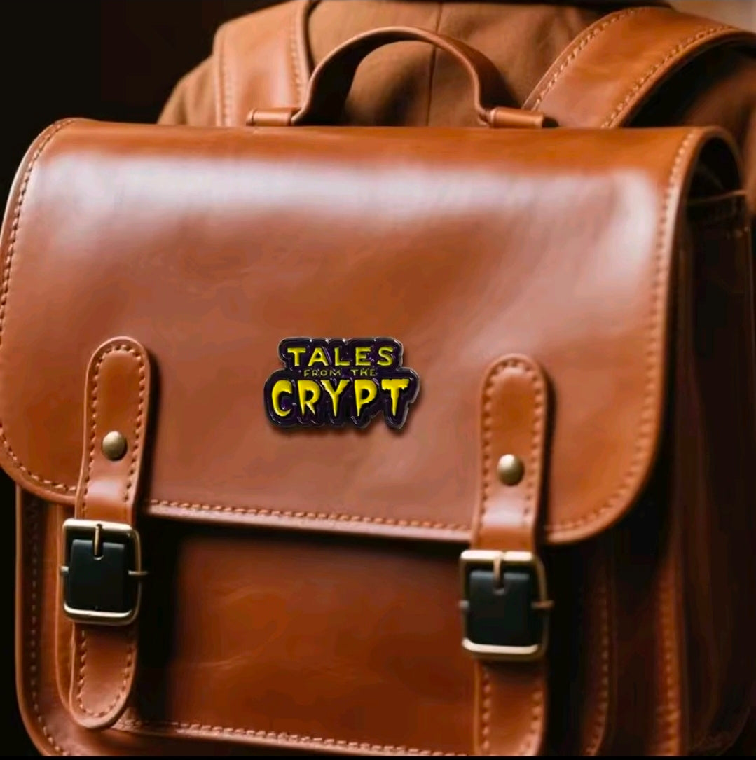 Tales from the Crypt enamel logo pin on tan leather bag, yellow and purple detail.