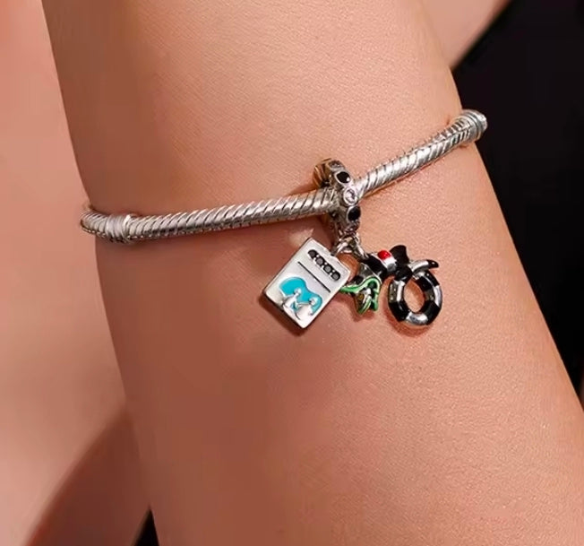 Wrist-worn S925 charm bracelet with teal square, black cauldron, and hoop ring dangles
