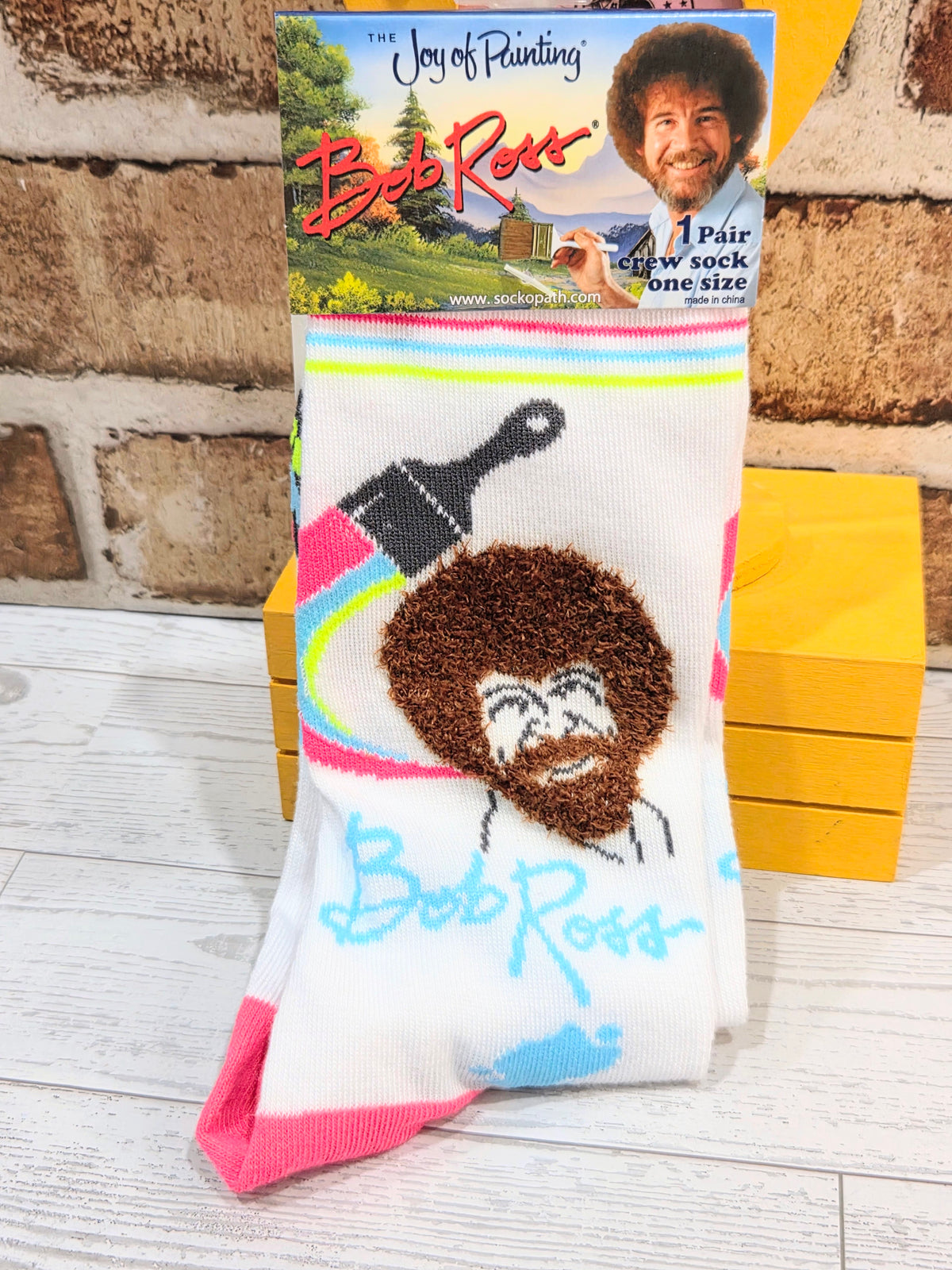 Pair of crew socks in retail packaging with Joy of Painting artwork and multicolor band