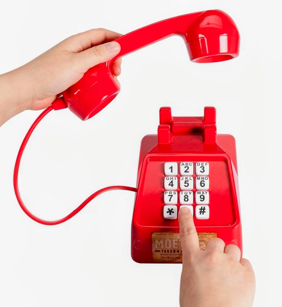 Hand holding red prank phone handset; keypad screen and Moe’s Tavern label shown