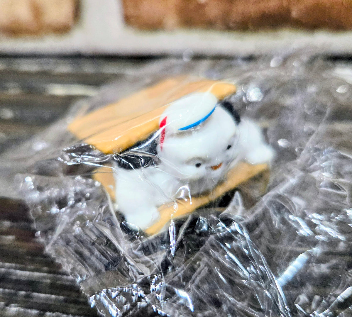 Toy mini figure with graham cracker and dark chocolate piece, angled view in clear plastic