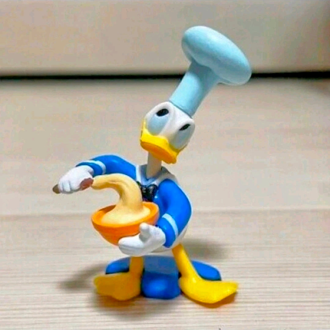 Donald Duck costume figure with light-blue hands and yellow shoes, holding an orange mallet