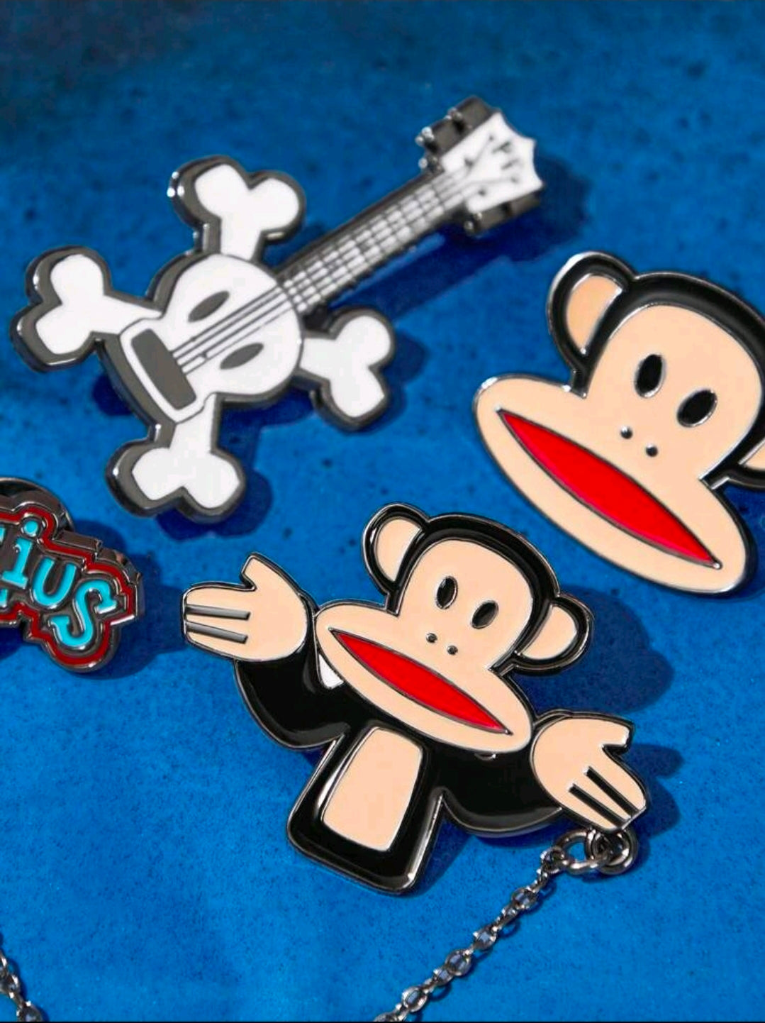 3-piece enamel pin set close-up: Julius monkey, white guitar, and Tutius logo pins