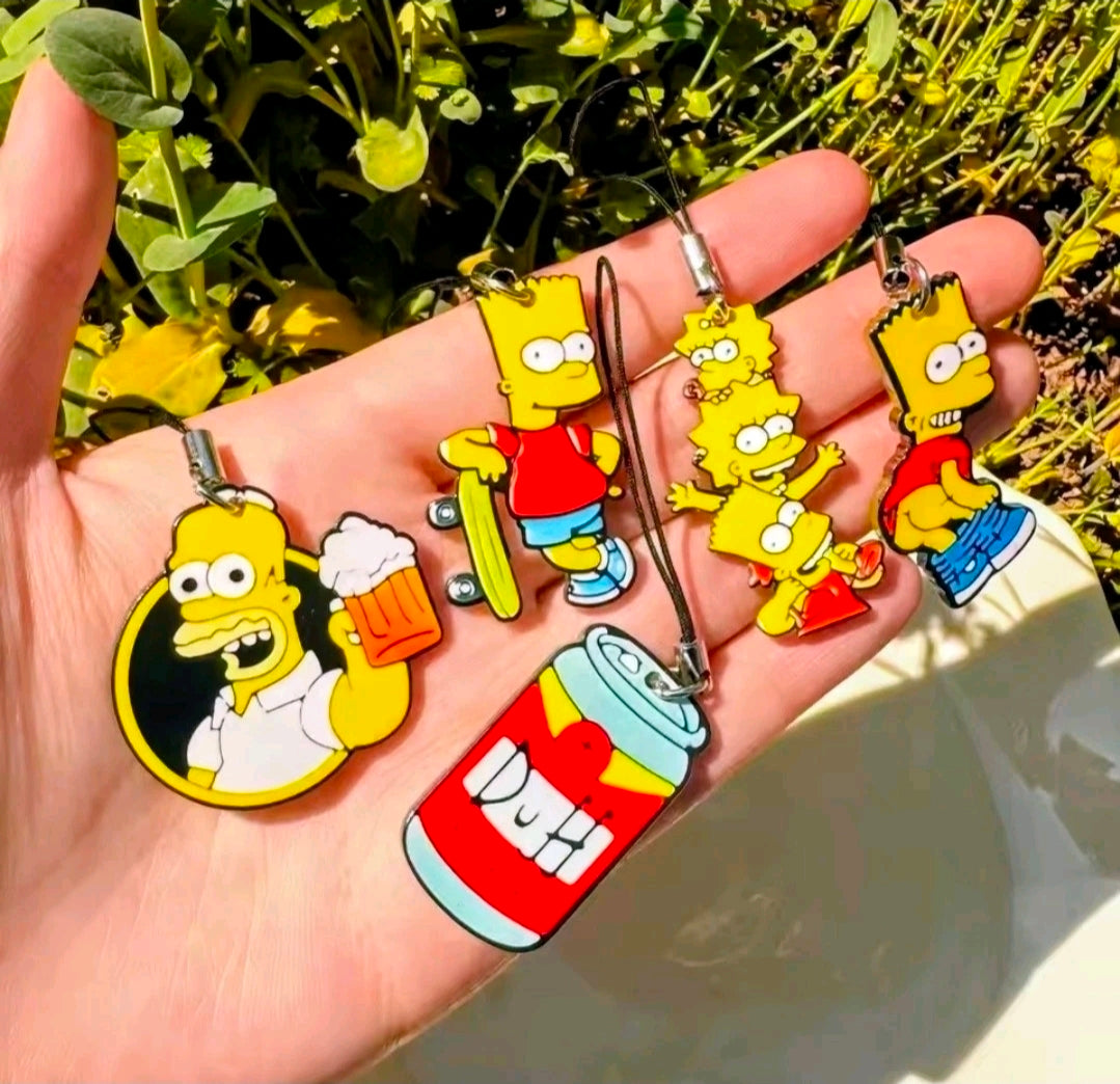 Five Simpsons character acrylic phone charms with black straps, held in a hand