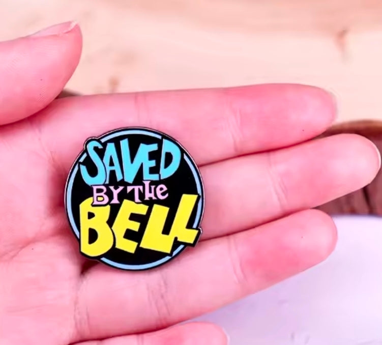 Round multicolor enamel pin logo on black background, held in a hand