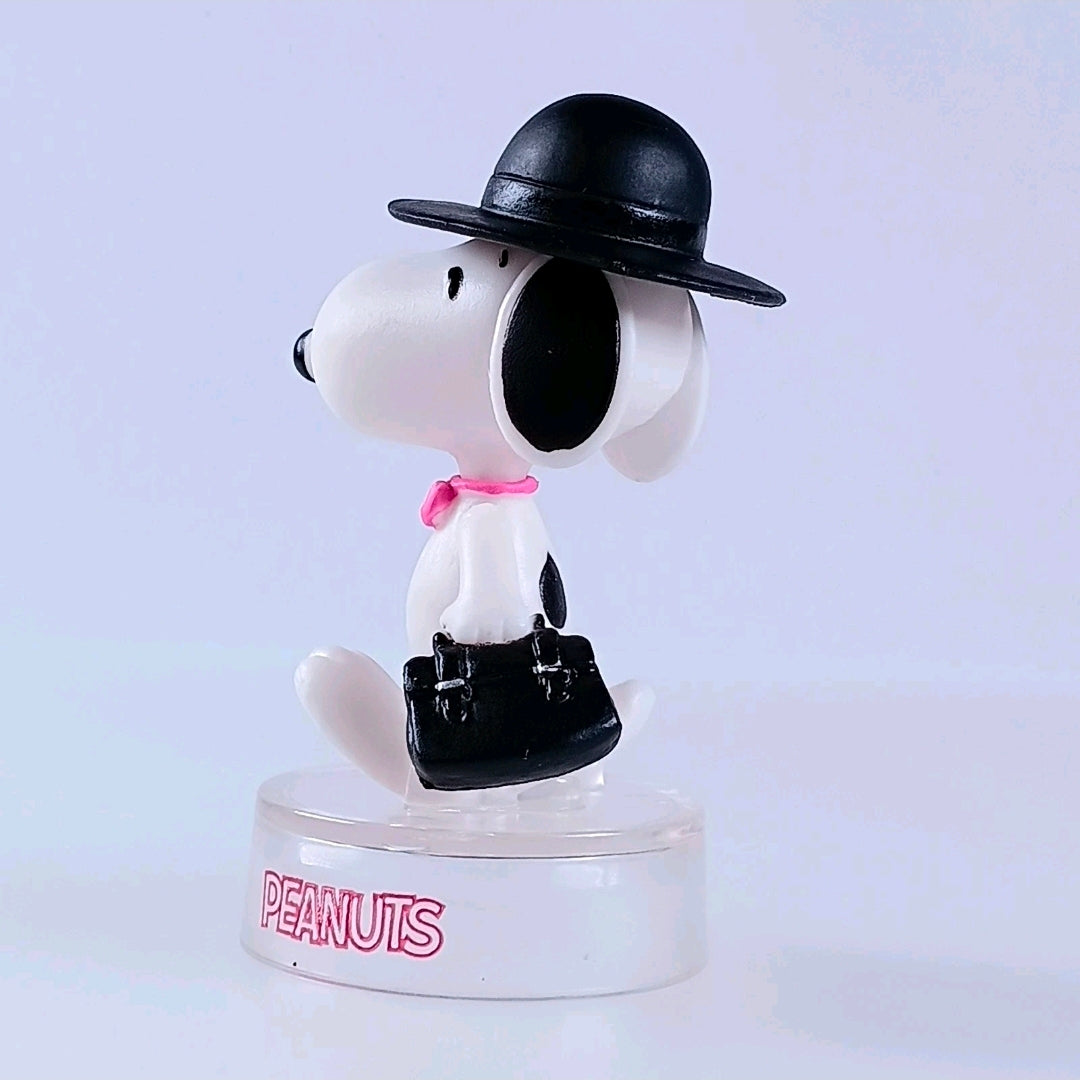 Snoopy figure wearing black hat and black bag, pink bow tie, clear PEANUTS base