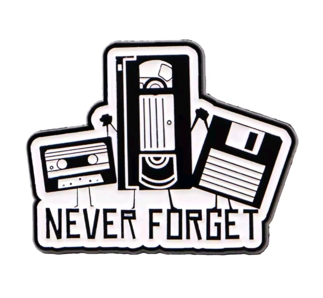 Enamel pin featuring a cassette, microphone, and 'Never Forget' text, black and white