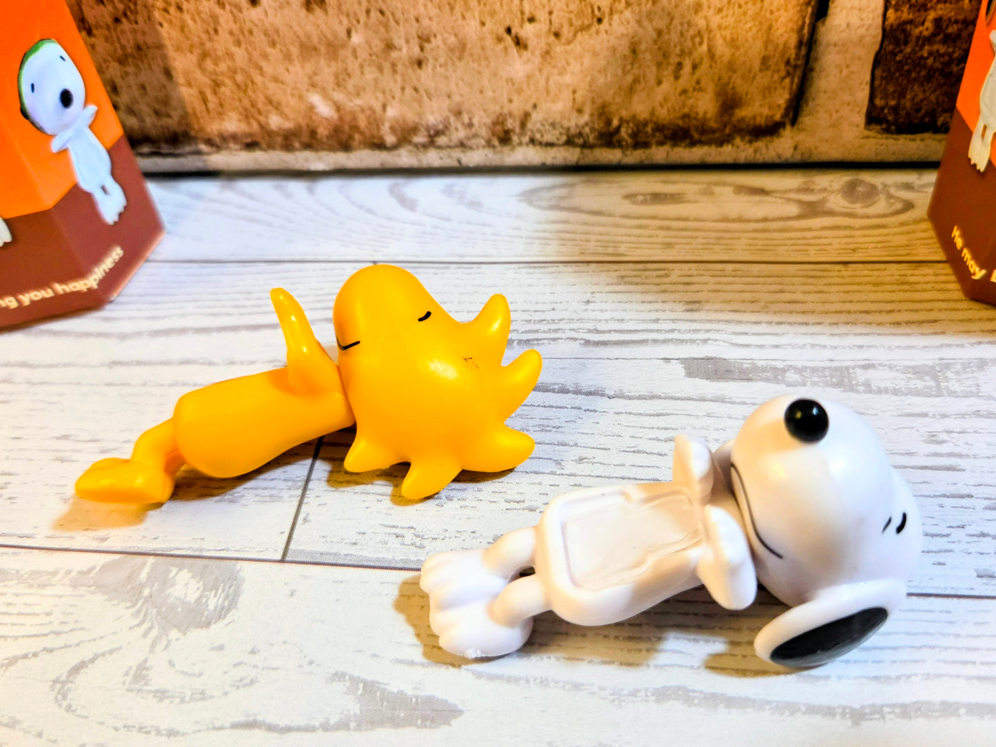 Mini vinyl character figures lying on light wood floor: yellow and white with black eyes