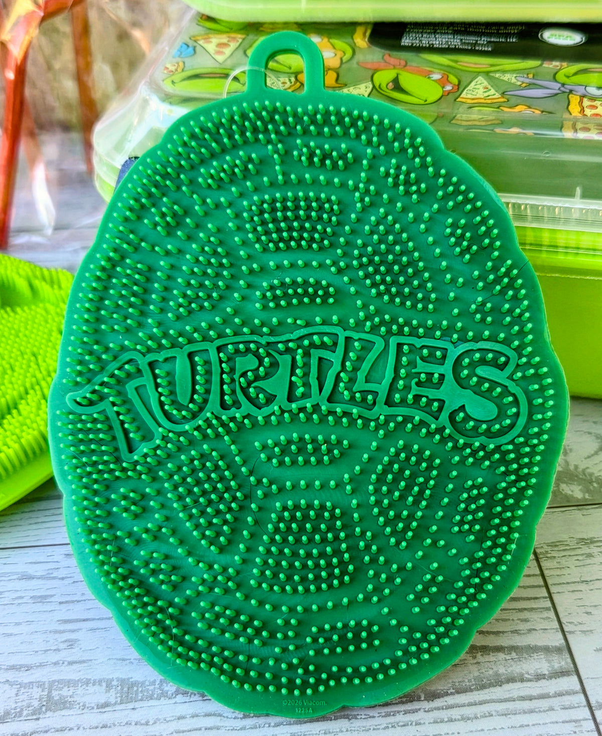 Round green silicone scrubber pad with raised Teenage Mutant Ninja Turtles lettering