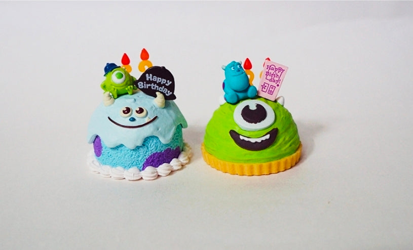 Two mini character birthday cakes with monster toppers, candles, and Happy Birthday signs