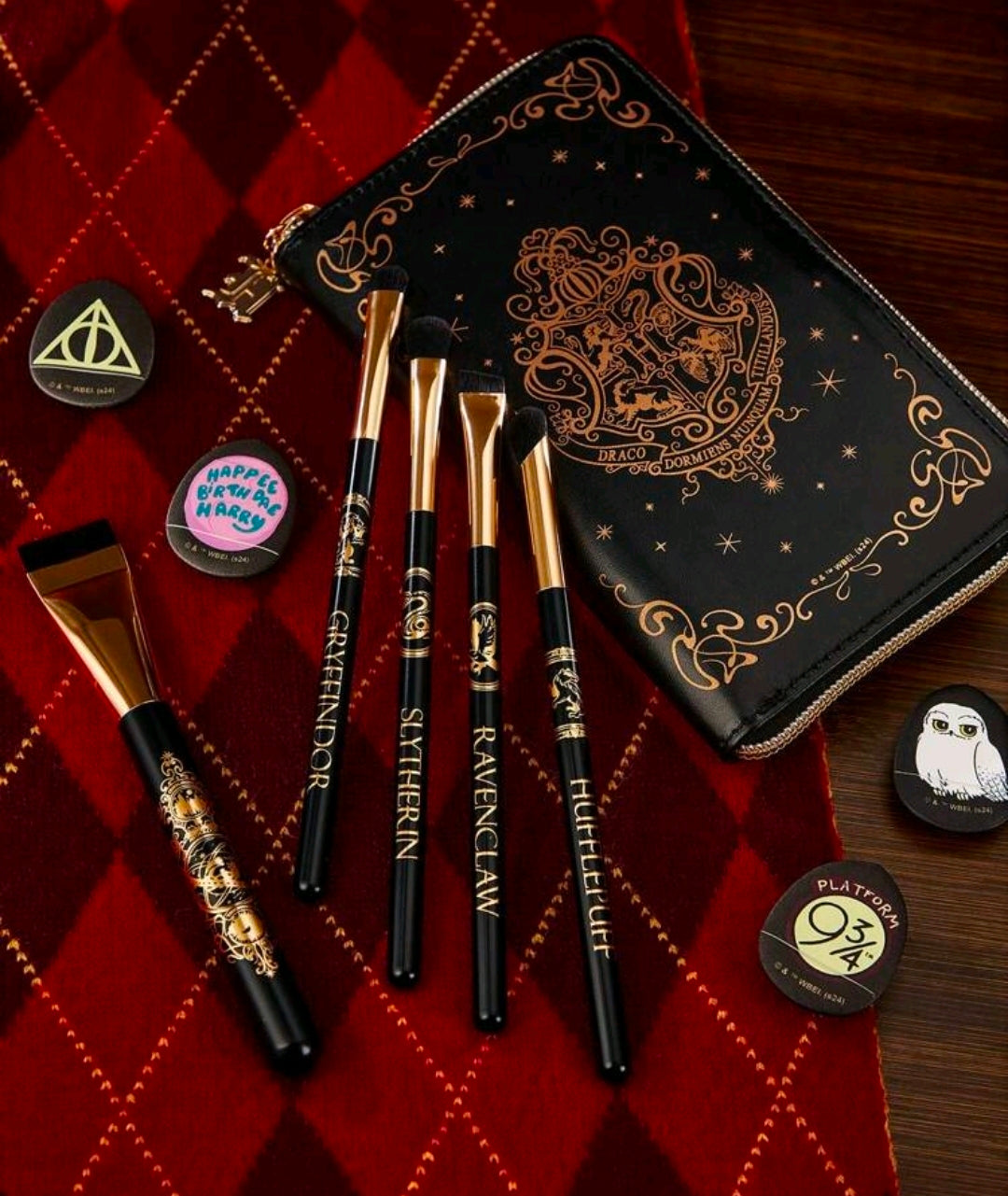 Gold-handled makeup brushes with illustrated black case and circular house badge pins